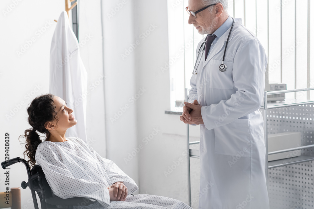 Obraz premium mature doctor talking to smiling african american woman sitting in wheelchair