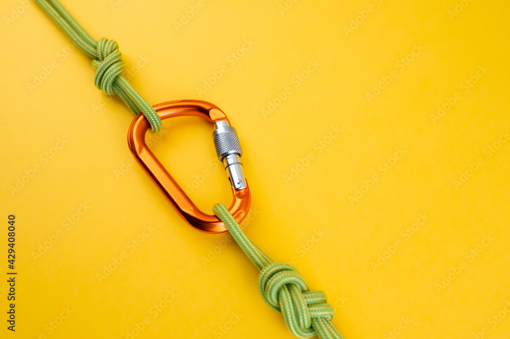 Orange Carabiner with rope. Equipment for climbing and mountaineering,  alpinism, rappelling. Safety rope. Knot eight. Isolated on the yellow  background. Minimal concept, copy space. Stock Photo