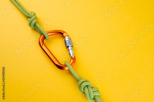 Orange Carabiner with rope. Equipment for climbing and mountaineering, alpinism, rappelling. Safety rope. Knot eight. Isolated on the yellow background. Minimal concept, copy space.
