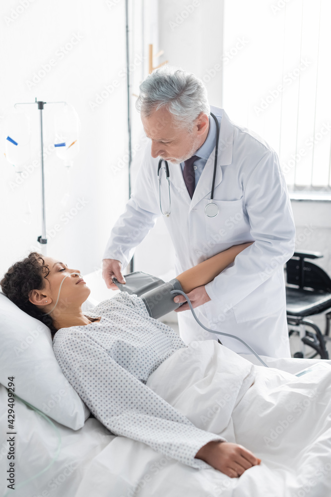 middle aged doctor going to measure blood pressure of african american woman in clinic middle aged doctor going to measure blood pressure of african american woman in clinic