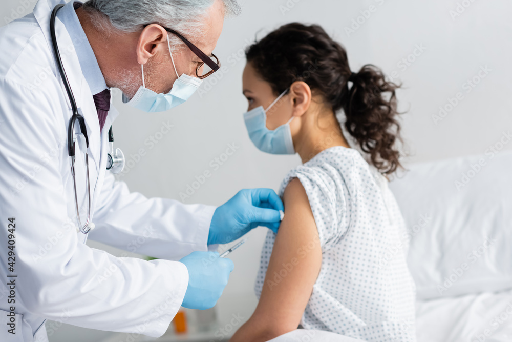 mature doctor in medical mask doing injection of vaccine to african american woman mature doctor in medical mask doing injection of vaccine to african american woman
