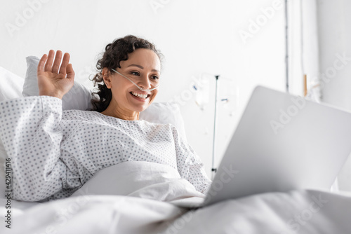 african american woman waving hand during video chat on laptop in hospital on blurred foreground