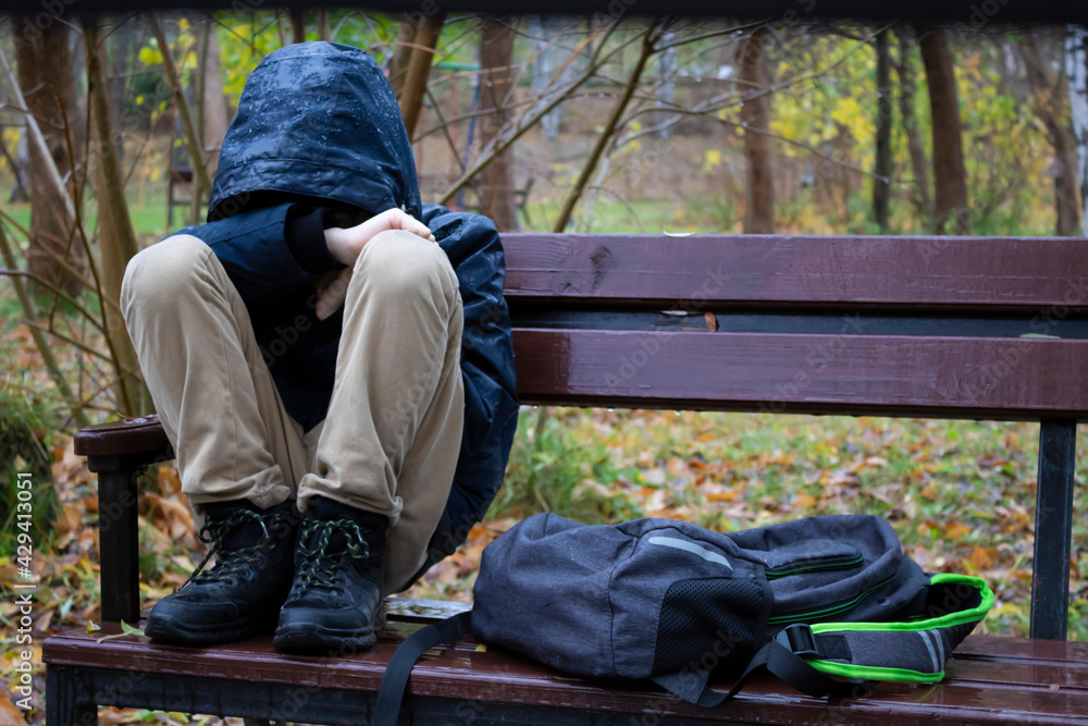 After school, a student upset in the park sits on a bench in an autumn park.