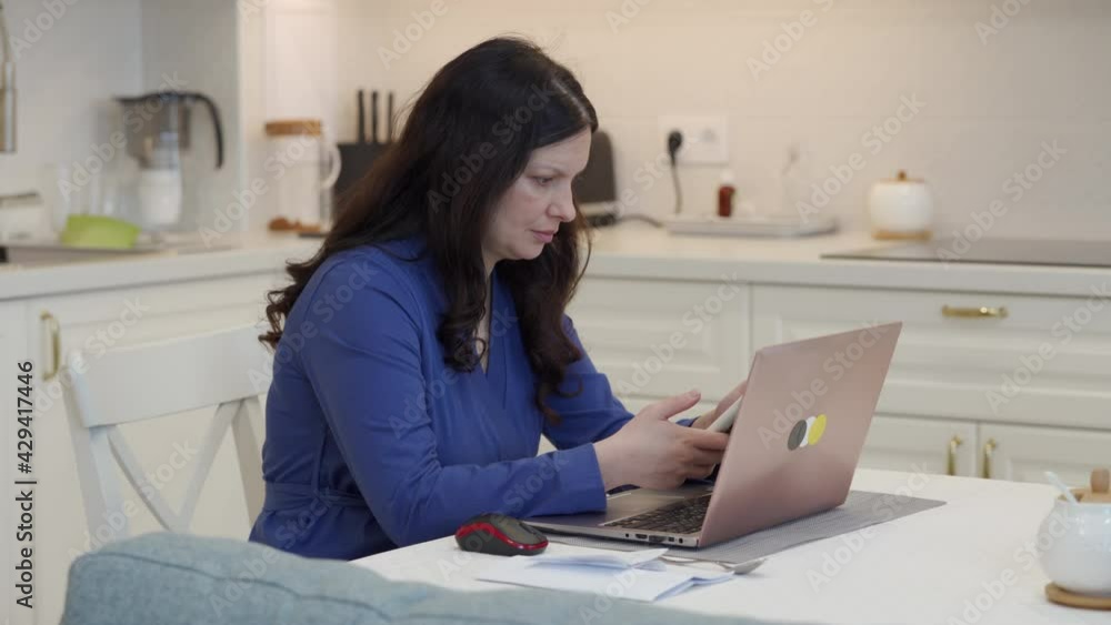 Woman working with laptop computer in the kitchen at home, white kitchen interior of modern apartment. High quality 4k footage Woman working with laptop computer in the kitchen at home, white kitchen interior of modern apartment. High quality 4k footage