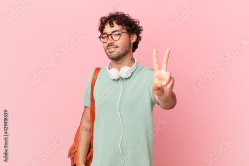 hispanic student smiling and looking friendly, showing number two or second with hand forward, counting down photo