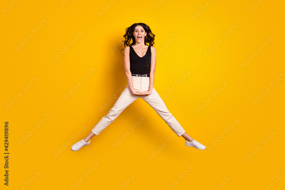 Full length body size photo of woman jumping high in stylish outfit smiling happy isolated on bright yellow color background Full length body size photo of woman jumping high in stylish outfit smiling happy isolated on bright yellow color background