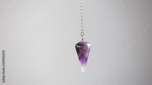 Purple Amethyst crystal pendulum hanging on chain on white background. photo