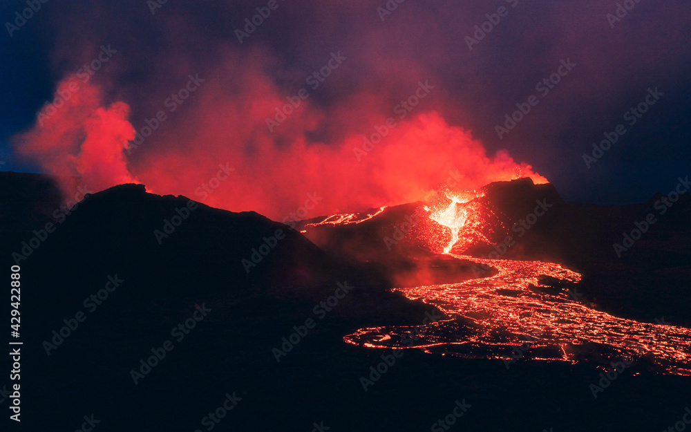 Lava erupting from the volcanic crater in the night in Iceland. Red smoke and blue sky. 