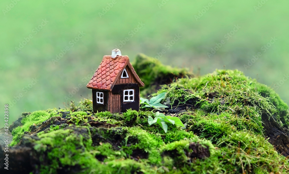 Toy house on moss, green natural forest background. Symbol of family, Mortgage, Real estate concept. Eco Friendly House.