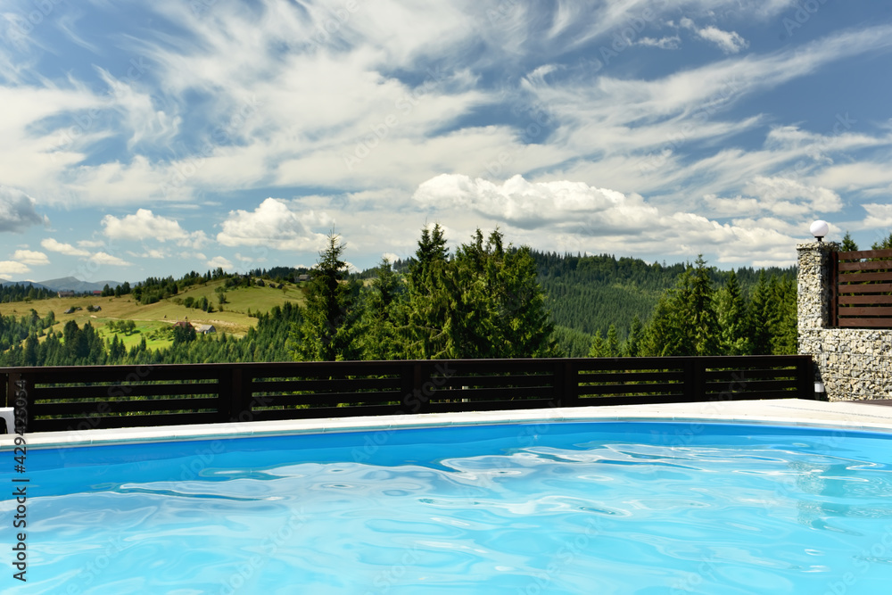 The pool overlooks the green mountains overgrown with fir trees on a sunny day.