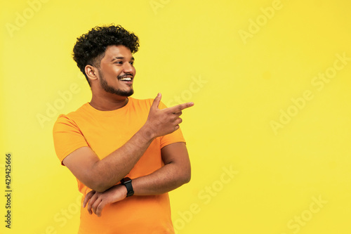 Foto Cheerful smiling man points to a place for text on a yellow background, he is wearing an orange T-shirt, good news