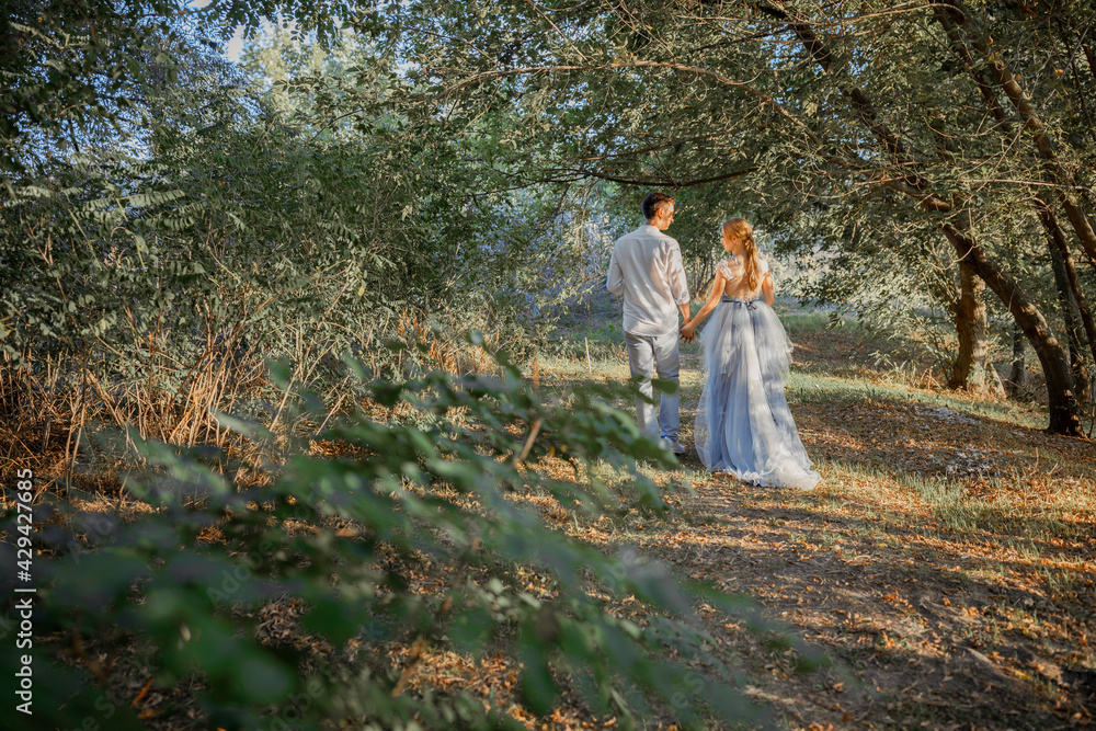 Happy young couple on a walk in the forest at sunset. The bride is wearing a blue wedding dress.