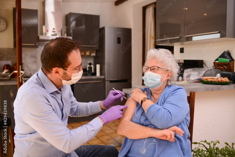 Fototapeta premium elderly senior woman with surgical mask having covid 19 vaccine injection by doctor male nurse at home