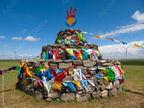 Heaps of stones (Aobao) build on a vast pasture in Xilinhot in Inner Mongolia. The Heaps has a lot of colorful prayer flags attached to it.Endless grassland. Blue sky with white clouds.Religious place photo