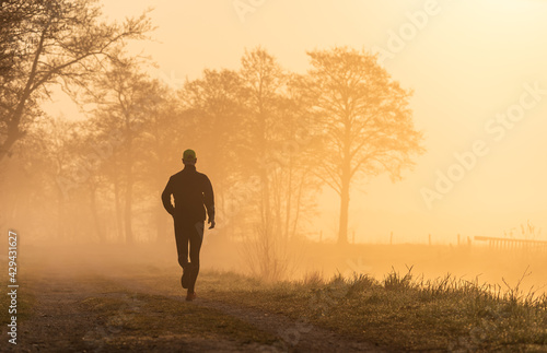 Silhouette of a man running during a foggy, spring sunrise in the countryside.