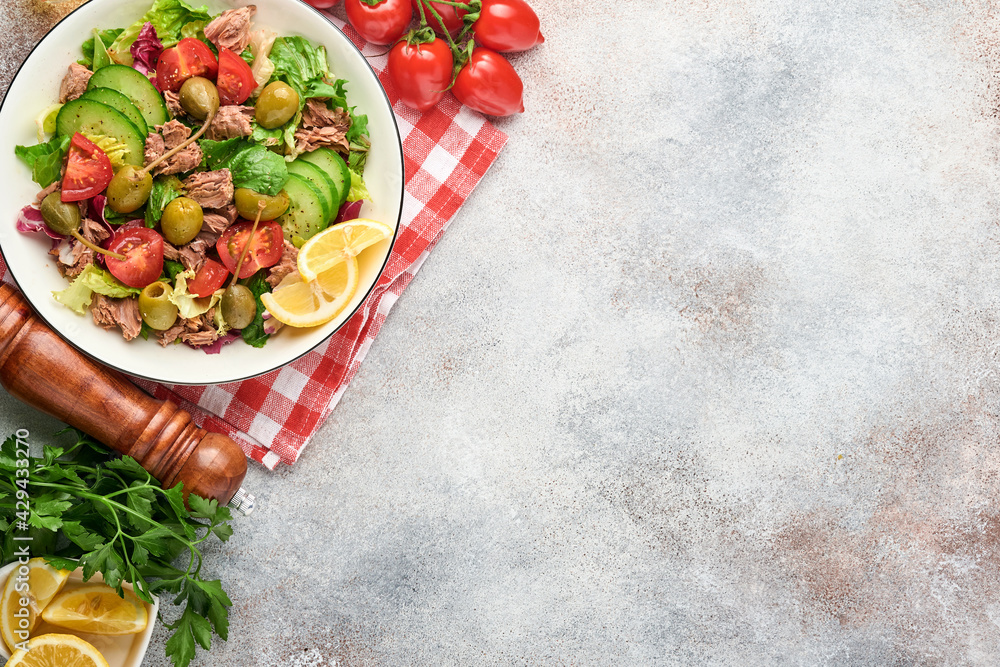 Tuna salad with fresh vegetables, olives, capers and lemon served in bowl on light grey background. Top view with copy space. Tuna salad with fresh vegetables, olives, capers and lemon served in bowl on light grey background. Top view with copy space.