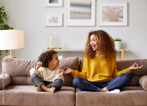 Happy afro american family mother and son in lotus pose meditating together in living room at home