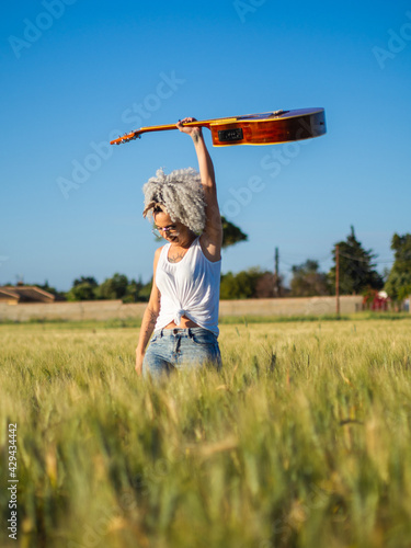 Mujer joven con una guitarra en un campo de trigo 