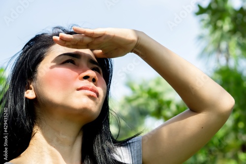 Asian woman having problem sunburn redness on face skin hand cover her face to protect ultraviolet from sunlight standing outdoors under sunny in summer 