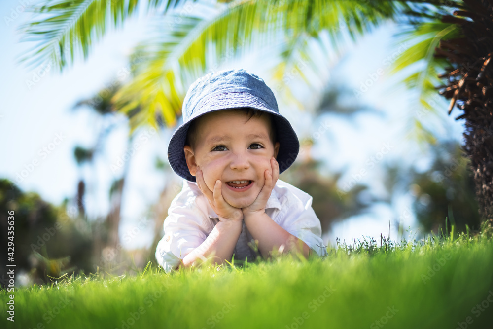Happy little boy laying on green grass under palms Happy little boy laying on green grass under palms