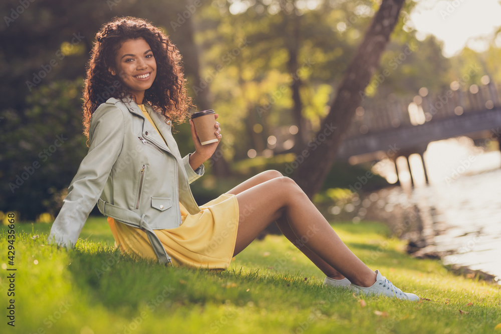Photo of lady sit grass hold cup takeout coffee look camera wear yellow dress footwear in green park outdoors Photo of lady sit grass hold cup takeout coffee look camera wear yellow dress footwear in green park outdoors