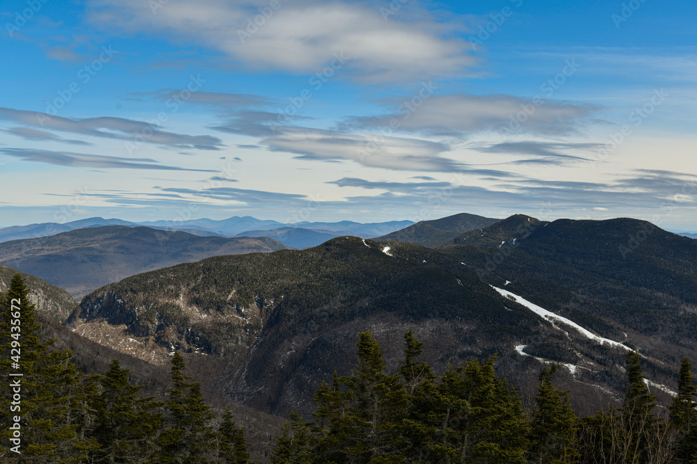 View from Mt. Mansfield Vermont at Stowe ski resort to Notch Path to Smugglers Notch. Late spring time with snow on the mountains and blue sky with clouds.