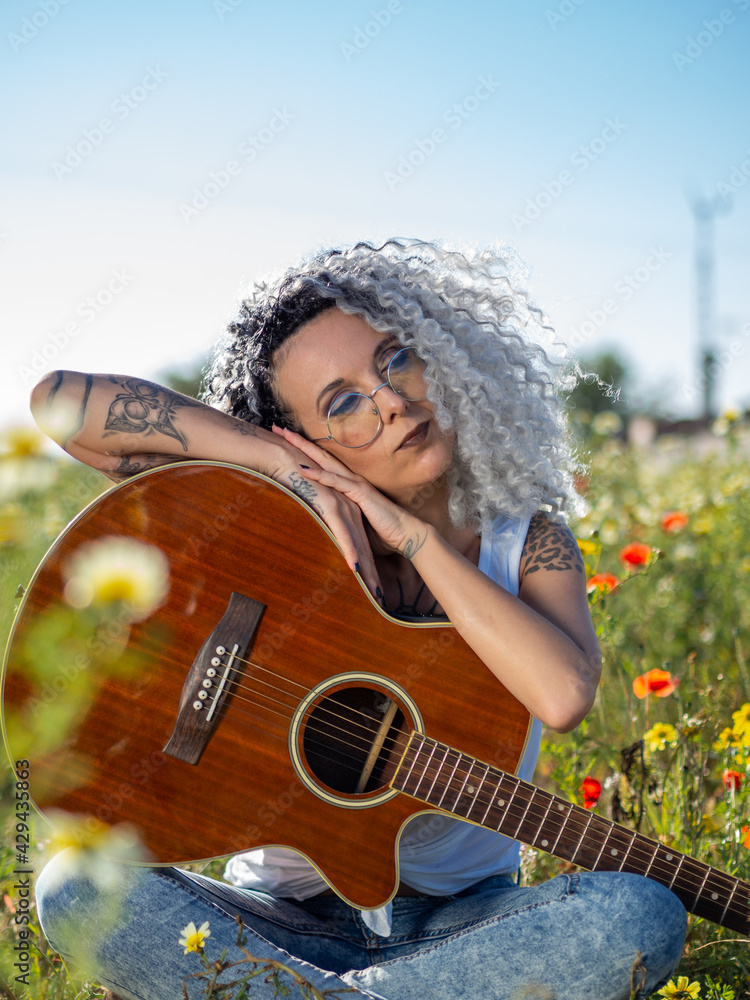 Mujer joven con tatuajes tocando la guitarra en un campo de margaritas foto  de Stock | Adobe Stock