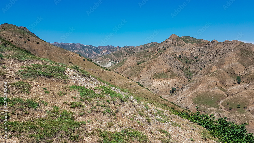 A panoramic view on Daqing mountains in Inner Mongolia. Endless mountain chains. The slopes are mostly barren, overgrown with small bushes and grass. Desolated landscape. Bio diversity of a region