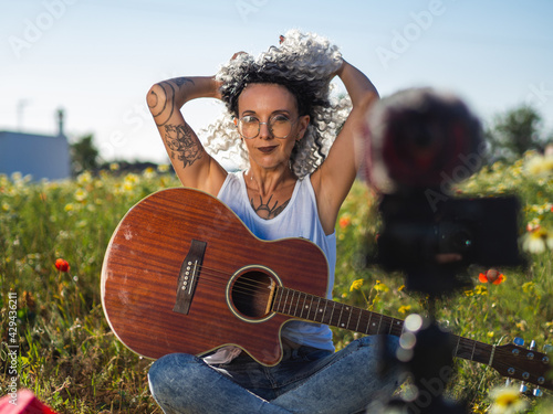 Mujer joven con tatuajes grabando un videoblog con la guitarra