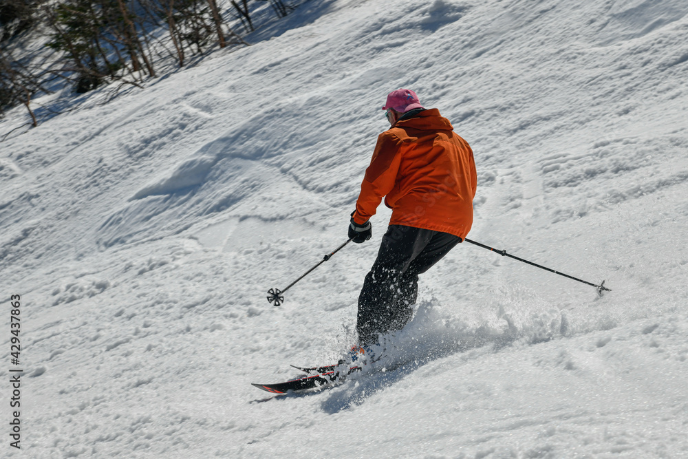 Freerider in orange jacket seen from behind making a turn in Stowe Mountain resort in Vermont during Spring in mid-April warm sunny day. Freerider in orange jacket seen from behind making a turn in Stowe Mountain resort in Vermont during Spring in mid-April warm sunny day.