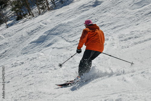 Freerider in orange jacket seen from behind making a turn in Stowe Mountain resort in Vermont during Spring in mid-April warm sunny day.