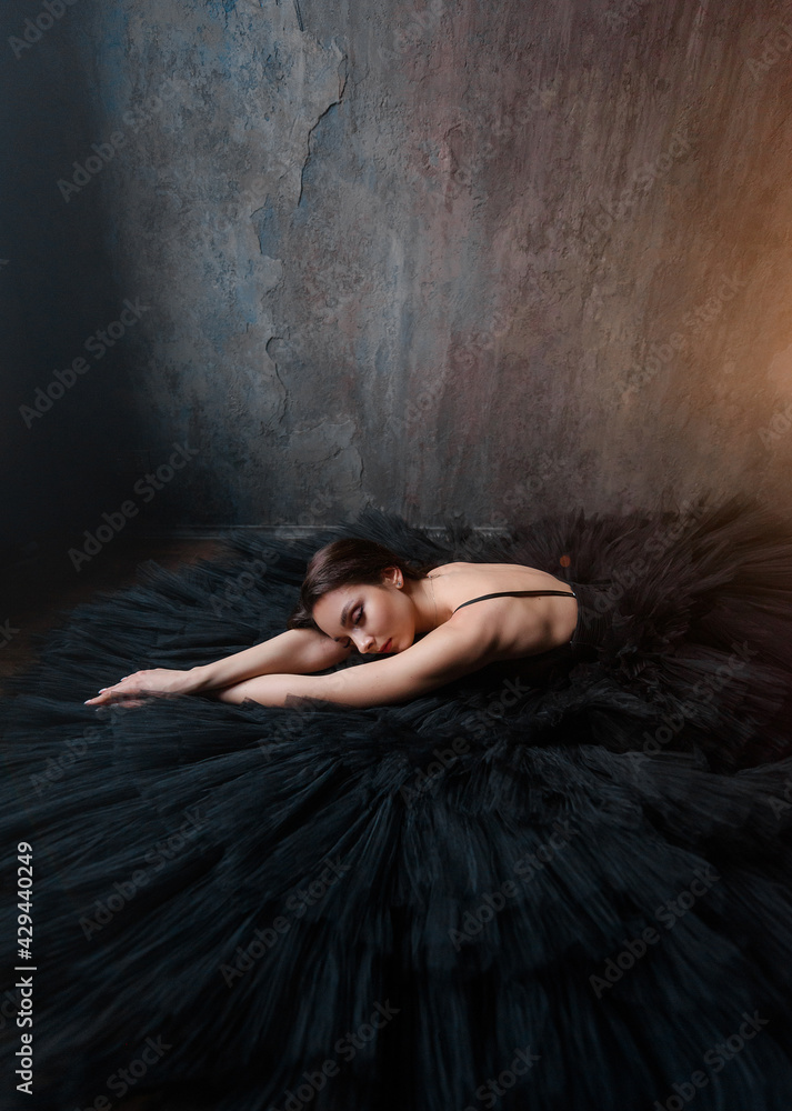 Side view of beautiful ballerina in a black dress lies near the wall. Concept of lush evening dresses