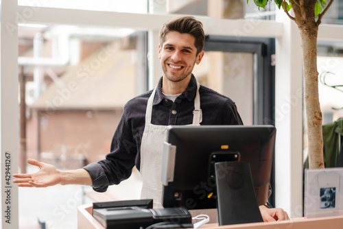 Smiling young man in apron standing at the cash register