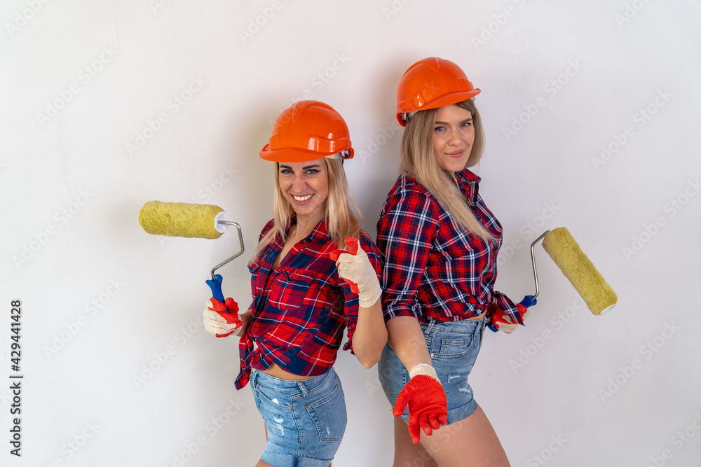 two pretty girls-painters in helmets and gloves with paint rollers in their hands two pretty girls-painters in helmets and gloves with paint rollers in their hands