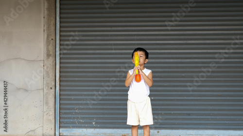 Asian child boy playing water gun toy at home in Songkran day with happy relaxing face. Concept of happy family activity at home, freedom fun. Songkran festival day 2021, new normal Covid 19.