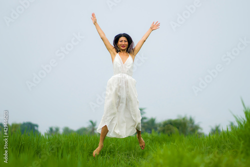 artistic portrait of young attractive and happy Asian woman outdoors at green rice field landscape wearing elegant long dress enjoying playful on beautiful nature 