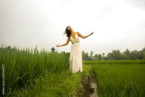 artistic portrait of young attractive and happy Asian woman outdoors at green rice field landscape wearing elegant long dress dancing on beautiful nature carefree 