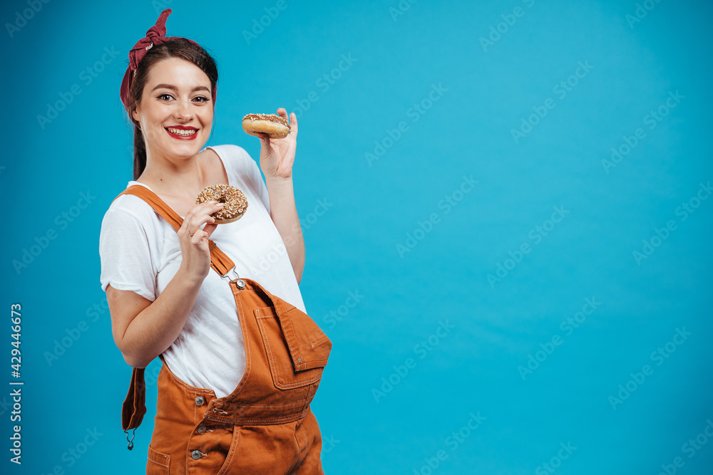Cheerful pregnant woman eating donuts dressed in pinup style