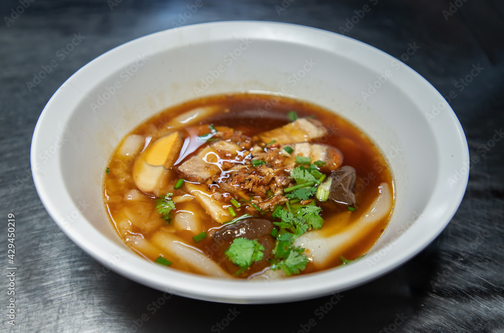 Chinese roll noodle soup with Crispy pork, Boiled egg, Pork blood Served on white bowl. Thai language called “Kuay Jab”, Asian food and street food in Thailand, Selective focus. Chinese roll noodle soup with Crispy pork, Boiled egg, Pork blood Served on white bowl. Thai language called “Kuay Jab”, Asian food and street food in Thailand, Selective focus.