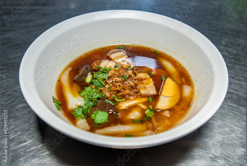 Chinese roll noodle soup with Crispy pork, Boiled egg, Pork blood Served on white bowl. Thai language called “Kuay Jab”, Asian food and street food in Thailand, Selective focus.
