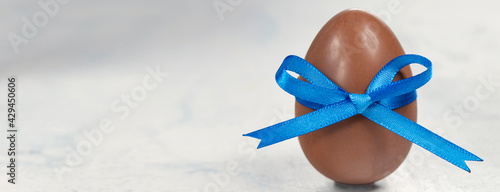 banner with Chocolate egg with a blue bow on a white concrete background.