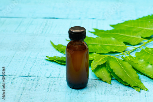 neem oil in bottle and neem leaf on blue wooden background.