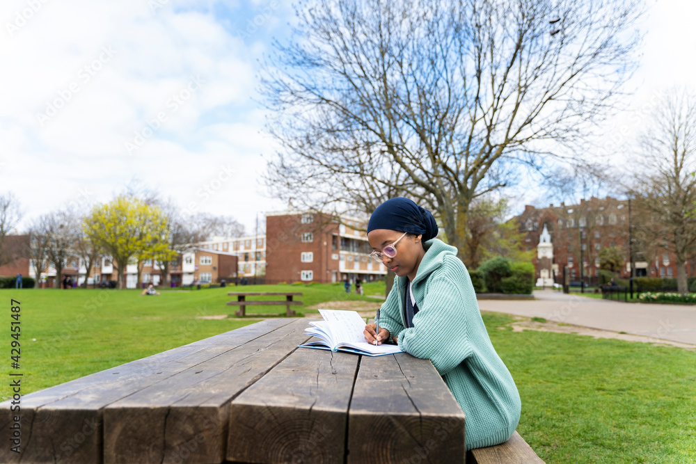 Fototapeta premium Black Muslim woman in park writing
