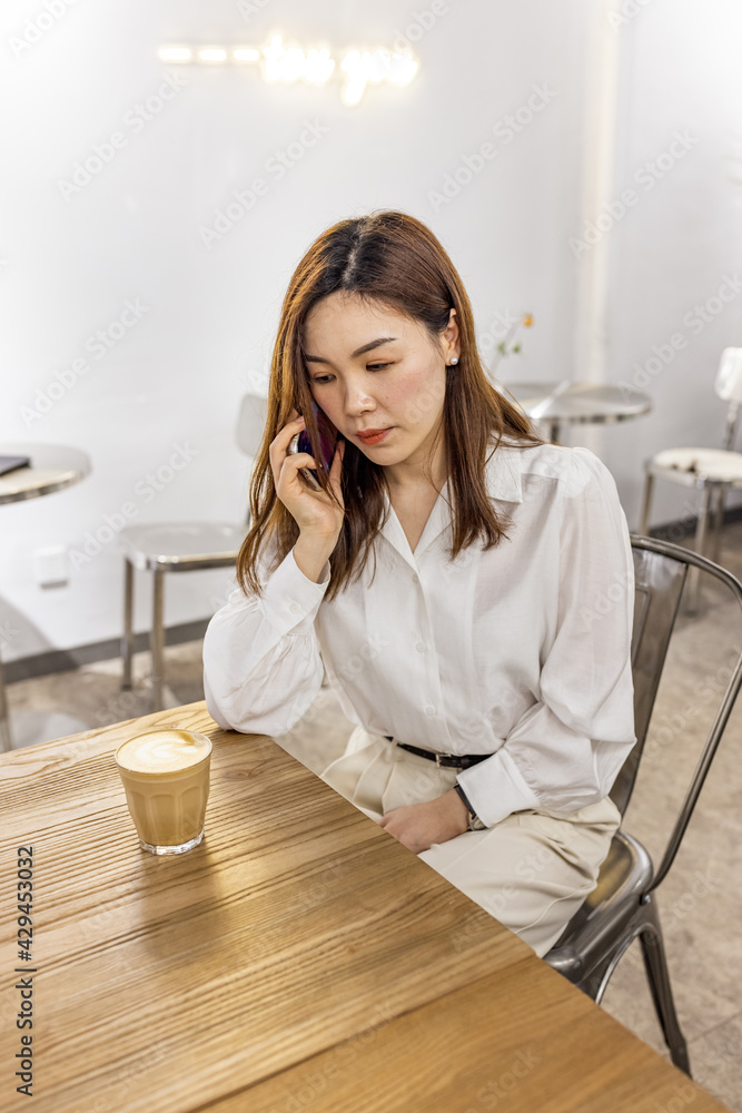 Smiling Asian Woman Talking On Cellphone In Cafe, Managing Her Business Schedule, Planning Meetings, Talking With Client or friends, Sitting At Table In modern Cafeteria Smiling Asian Woman Talking On Cellphone In Cafe, Managing Her Business Schedule, Planning Meetings, Talking With Client or friends, Sitting At Table In modern Cafeteria