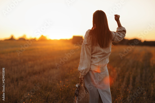 young woman in the beautiful light of the summer sunset in a field is walking near the straw bales. beautiful romantic girl with long hair outdoors in field.