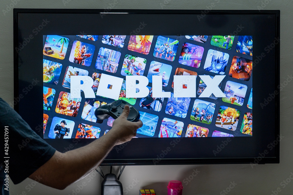 Foto de man with a controller standing in front of a PC console TV screen  with a steam controller playing popular free to play game Roblox do Stock