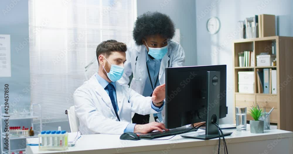 Portrait of multi-ethnic healthcare workers colleagues working in medical center browsing on computer. Caucasian male doctor typing on computer and talking to African American woman co-worker Portrait of multi-ethnic healthcare workers colleagues working in medical center browsing on computer. Caucasian male doctor typing on computer and talking to African American woman co-worker
