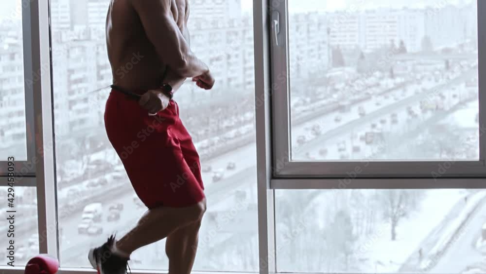Muscular shirtless man jumps over rope in studio with panoramic windows - boxer gloves on the floor Muscular shirtless man jumps over rope in studio with panoramic windows - boxer gloves on the floor