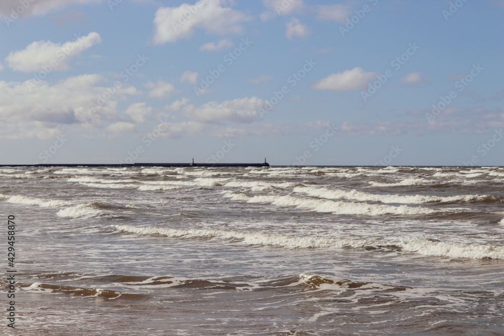 Sea waves under blue clody skies with pier in the distance Sea waves under blue clody skies with pier in the distance