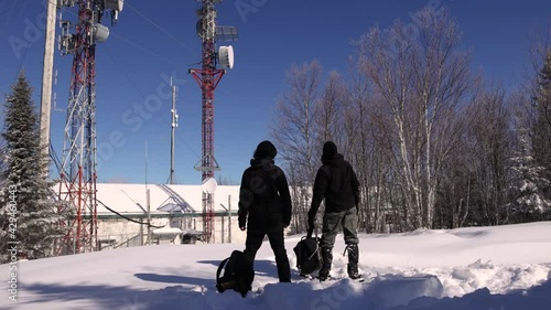 Locked down shot of two young tourists taking a look at cellular communication towers for signal transmission, located in the snowy hills. photo